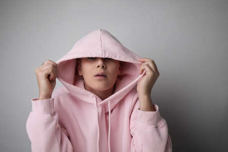 Close-up of young bald woman wearing pink hoodie posing at studio.