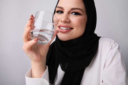 Cropped portrait of happy muslim woman wears hijab drinking water. Isolated.の写真素材