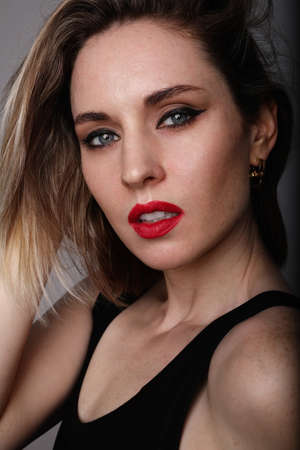 Vertical close-up of young woman, wears black t-shirt, posing at the studio.
