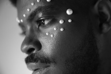 Black and white image of handsome black man with pearls on his face.