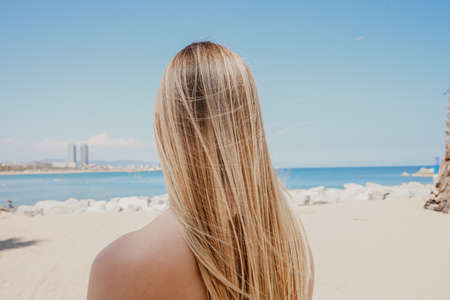 Back of blonde long-haired young woman walking on the beach in sunny day.の写真素材