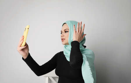 Young Arabian woman with happy smile using smartphone, isolated on white wall.の写真素材