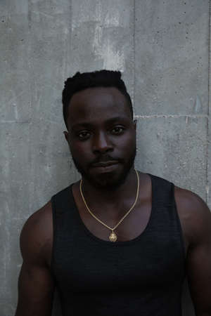 Vertical headshot of black man doing workout outdoor, posing on grey background.