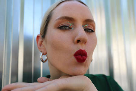 Close-up of young attractive blonde woman, sending air kisses, over shiny wall.の写真素材