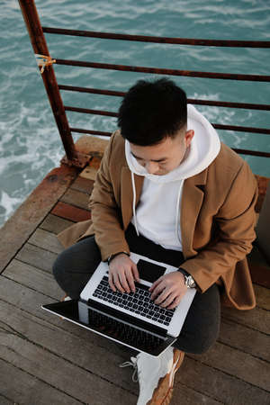 Asian businessman using laptop on the beach. Outdoor. Vertical image.