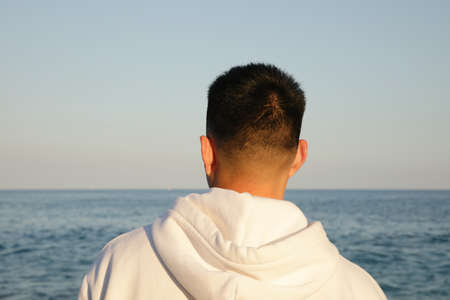 Young asian man standing against nature landscape in deep thought. Back view.の写真素材