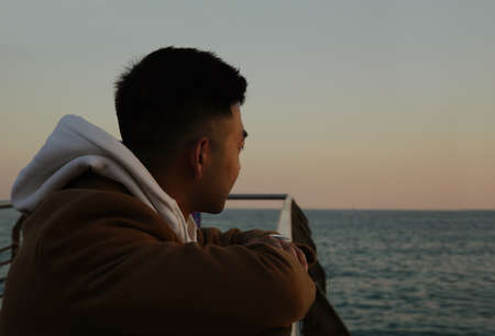 Young asian man standing against nature landscape in deep thought.の写真素材