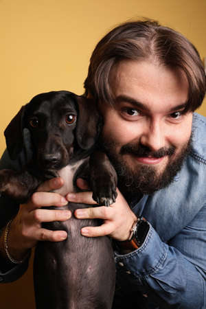 Bearded hipster posing over yellow background with dog. Vertical.