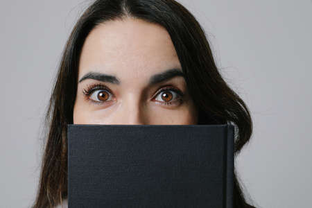 Close-up of middle-aged woman covering face with diary. Looking at the camera.の写真素材