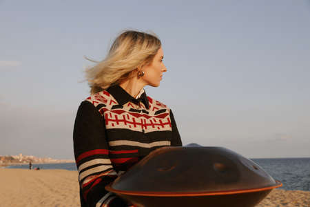 Young woman plays hang drum handpan while sitting on the beach. Relax and calm.の写真素材