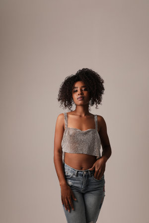 Beautiful young black woman posing on grey wall, looking at the camera. Vertical