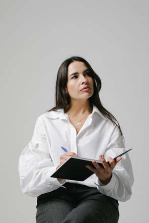 Middle-aged businesswoman, mentor coach over white wall writing in her notebook.