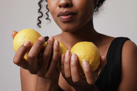 Cropped portrait of dark skinned girl with fruits lemon. Vitamin C concept.