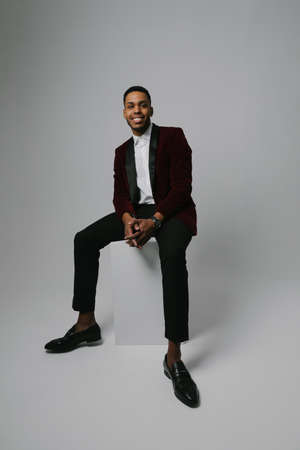 Full-length shot of black man wearing brandy suit posing over grey background.
