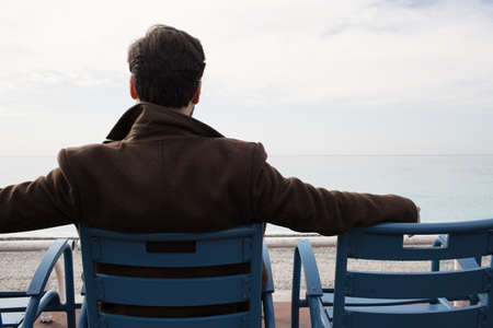 Back view of man in coat sitting on the bench against the sea coast. Cropped.の写真素材