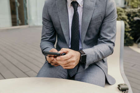 Cropped photo of businessman using his smartphone, sitting outdoor.の写真素材