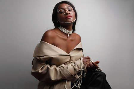 Beautiful African black woman with pearls on her skin posing over grey wall.