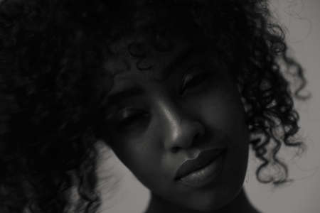 Portrait of beautiful young black woman on grey wall, black and white image.