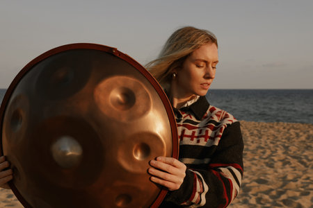 Woman holds hang drum handpan while sitting on the beach. Meditation mood.