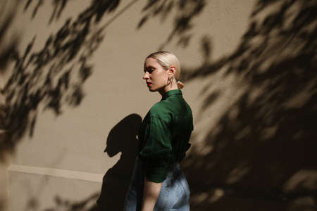 Portrait of young blonde woman posing on beige wall with dark shadows.の写真素材