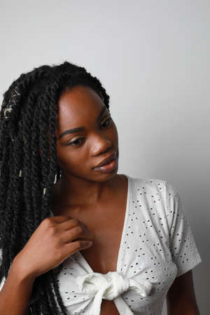 Attractive young African woman with braids posing over white wall. Vertical.