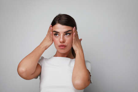 Beautiful young woman doing face massage over white wall in the studio.の写真素材