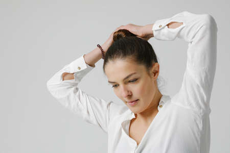 Joyful woman dressed in casual shirt, making hair bun looking aside.