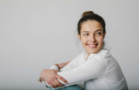 Woman smiling and looking aside, dressed in casual shirt, poses on white wall.の写真素材