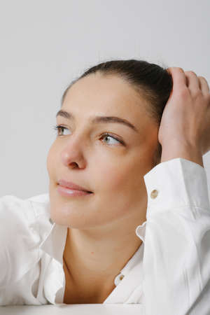 Close-up of woman looking aside, dressed in casual shirt, poses on white wall.