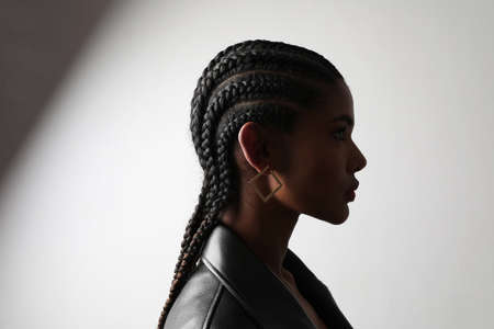 Side portrait of African young woman with braids posing on white wall.