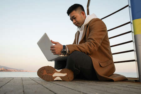 Relaxed young Asian man using laptop on the beach.