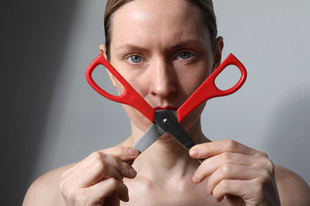 Young woman with scissors looking at the camera posing on white background.の写真素材