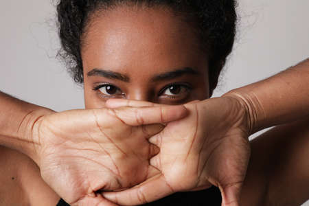 Close-up portrait of African American young woman covers her face with hands.の写真素材