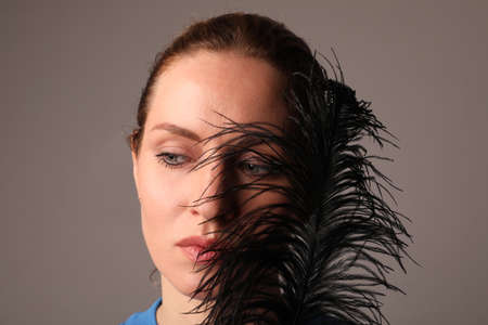Beauty woman holds a black feather posing on dark background. Mock-up.