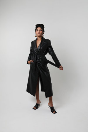 Young African American woman wears black long jacket posing indoor. Mock-up.の写真素材