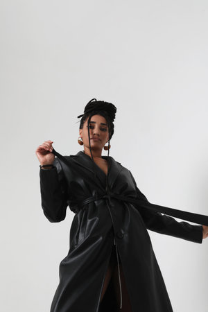 Young African American woman wears leather long jacket posing indoor. Mock-up.の写真素材