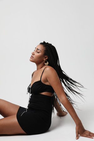 African American woman with long dark braids, posing over white wall. Vertical.の写真素材
