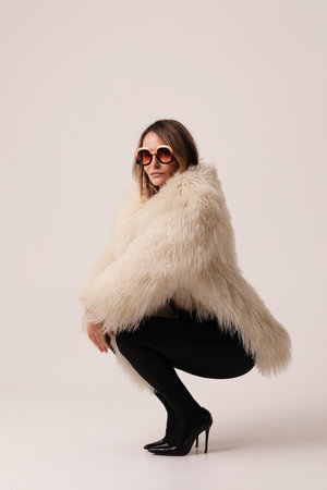 Vertical portrait of young woman wearing white fur coat posing indoor. Mock-up.の写真素材