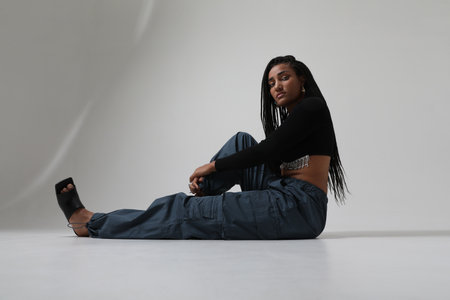 African American young woman with long dark braids, sitting on white floor.の写真素材