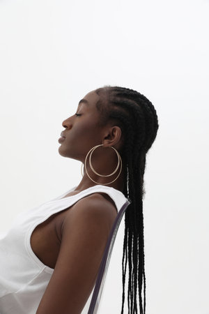 Side portrait of young African woman with long braids, wearing golden hoops.