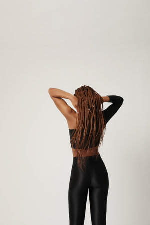 Young African American woman with long braids posing on white wall. Back view.の写真素材