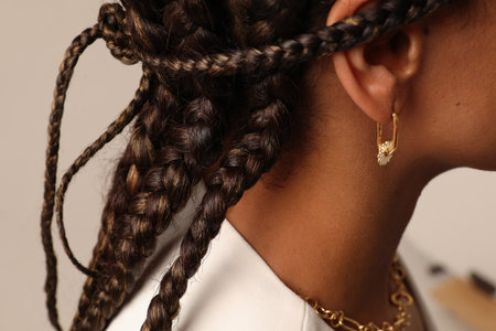 Cropped portrait of woman with a black braids wearing golden tiny earrings.の写真素材