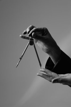 Cropped image of female hands holds the compasses over grey studio background. Black and white.の写真素材