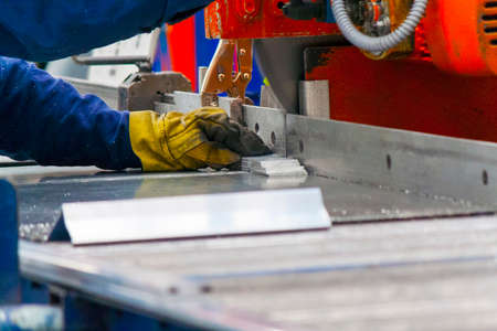 Hands with yellow gloves cutting thin core of aluminum alloy with a big saw