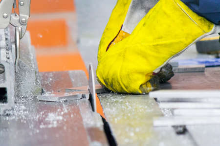 Hands with yellow gloves cutting thin core of aluminum alloy with a big saw
