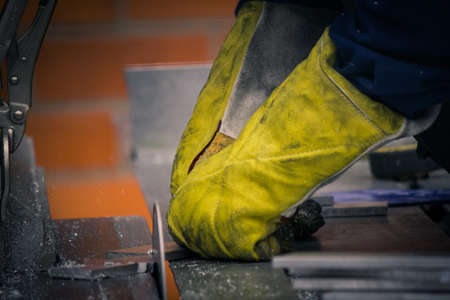 Hands with yellow gloves cutting thin core of aluminium alloy with a big saw