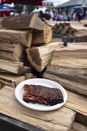 A paper plate of a half-rack barbecue ribs on a pile of firewood at The Great New York State Fair.