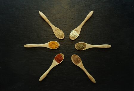 Photography of powder spices in little wooden spoons on a slate for food background