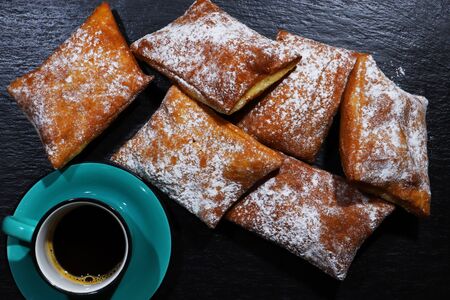 Photograph of New-Orleans style beignets and a cup of coffee on a slate