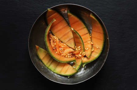 Photography of melon peels and seeds in a stainless steel bowl on slate background for food illustrationsの写真素材